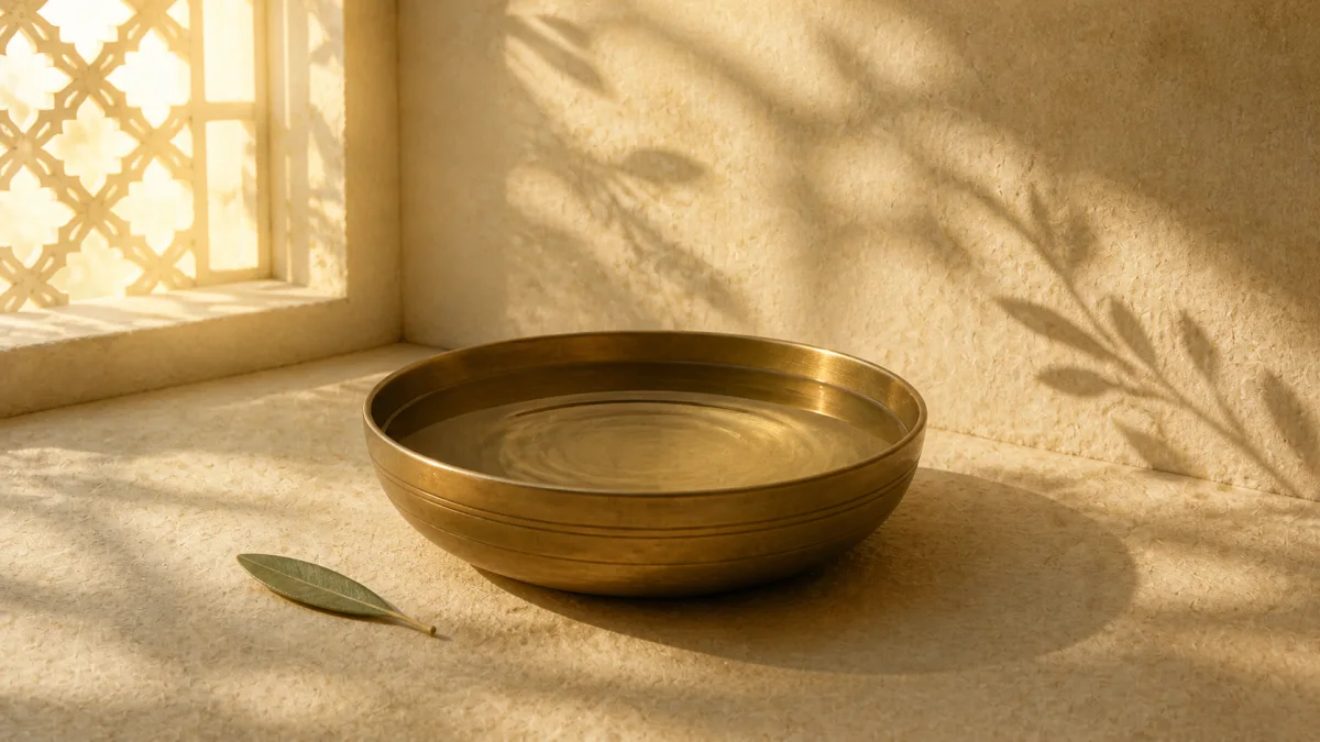 A brass bowl of nearly still water in warm window light